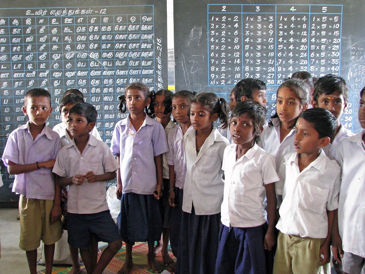 Schoolchildren standing in front of chalkboards in a classroom.
